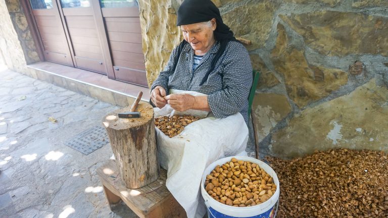 Močiutė nedidelio kaimo gatvėje gliaudanti migdolus. Kreta, Graikija | Mano Kreta